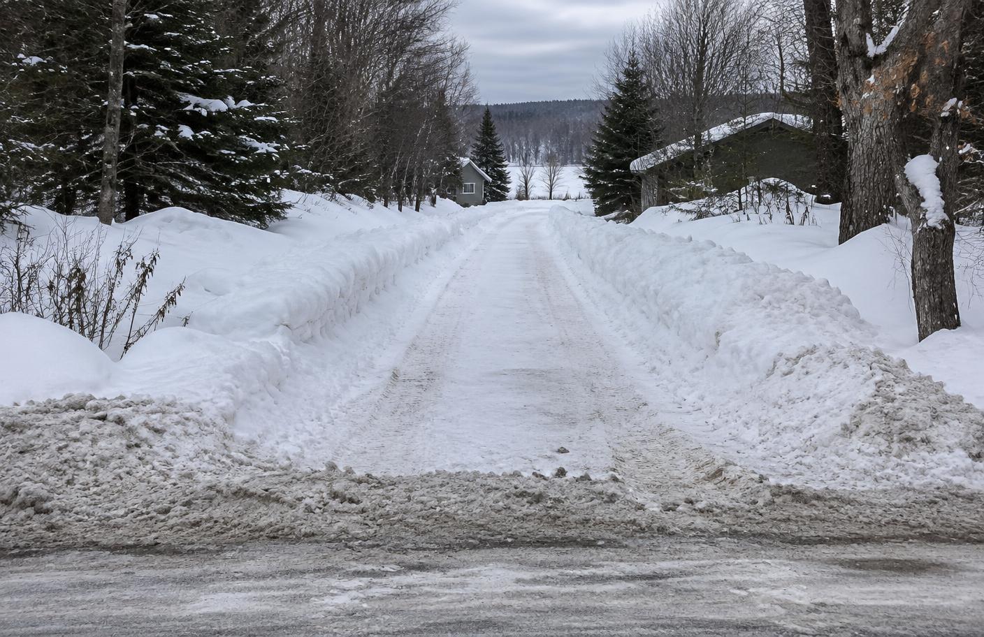 Conventionally plowed cottage lane with high snowbanks and a windrow at the road.